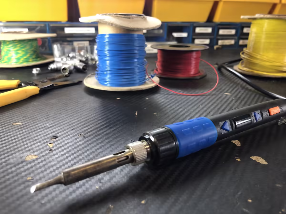 A soldering iron in the foreground with spools of cable behind on our maintenance desk