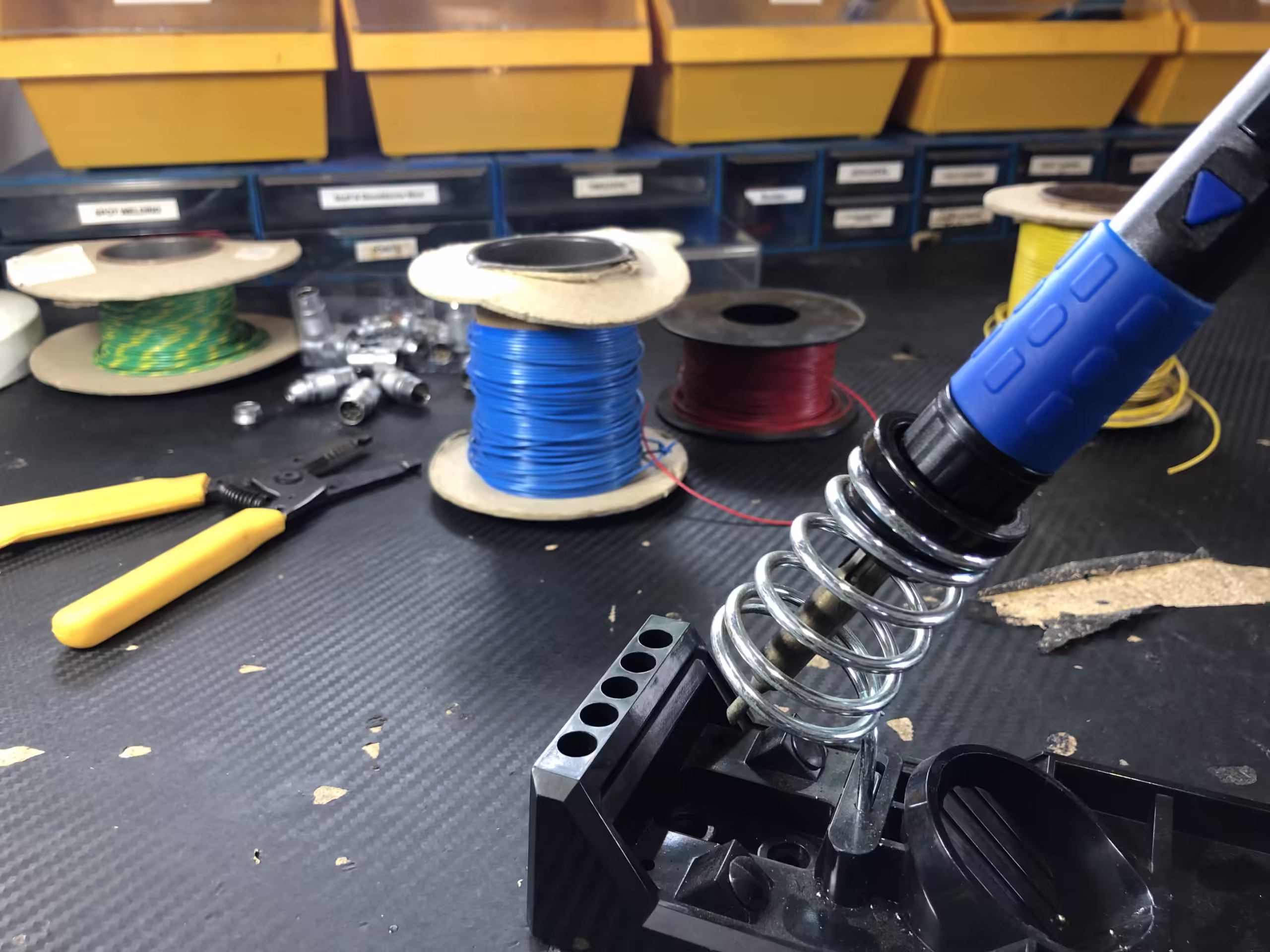 A soldering iron in the foreground with spools of cable behind on our maintenance desk